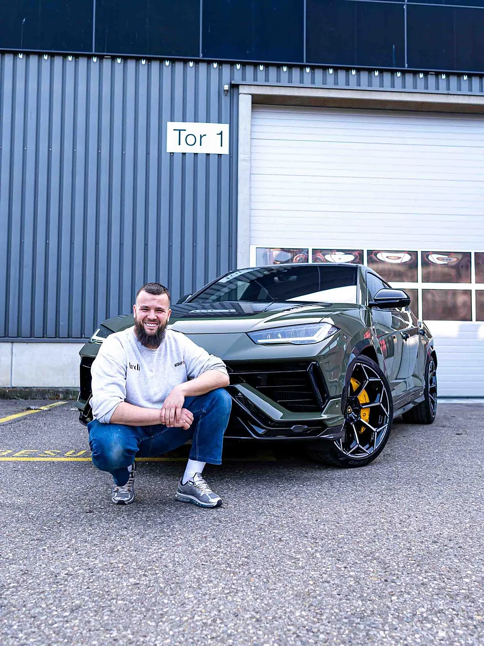 Ardian Fetahu, in der Hocke vor einem grünen Lamborghini Urus an Tor 1 der Halle